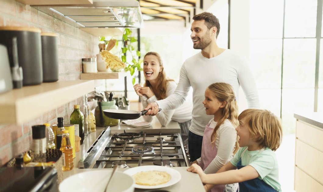 Fröhliche Familie mit zwei Kindern in Küche beim gemeinsamen Kochen stehend