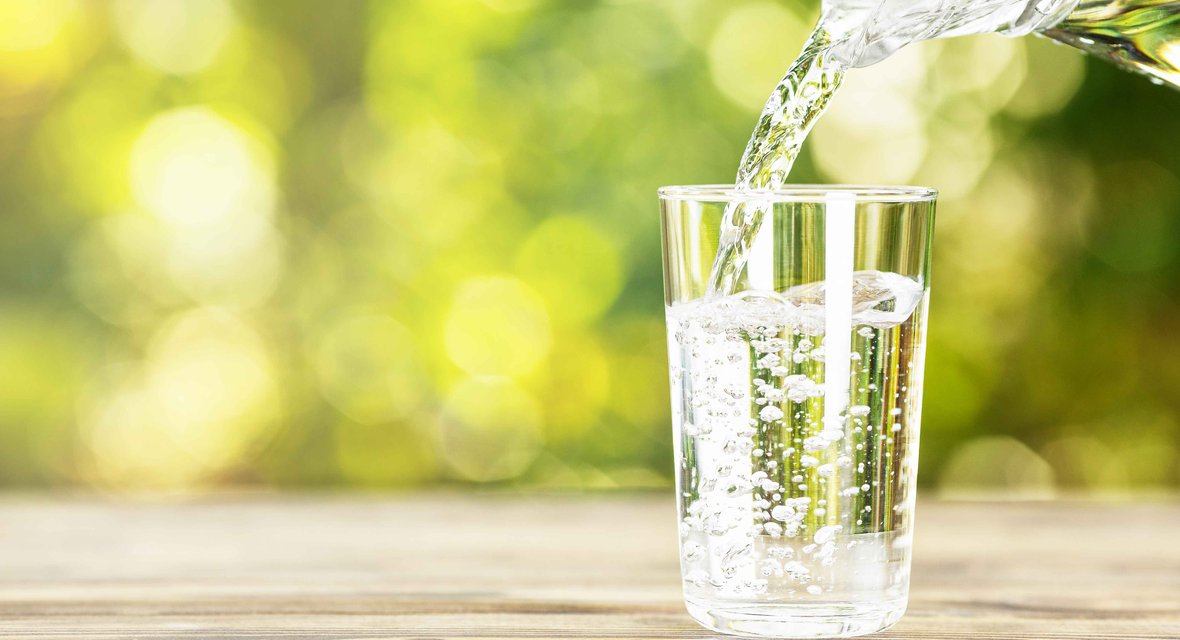 Wasserglas wird mit frischem Trinkwasser aus Glaskrug gefüllt