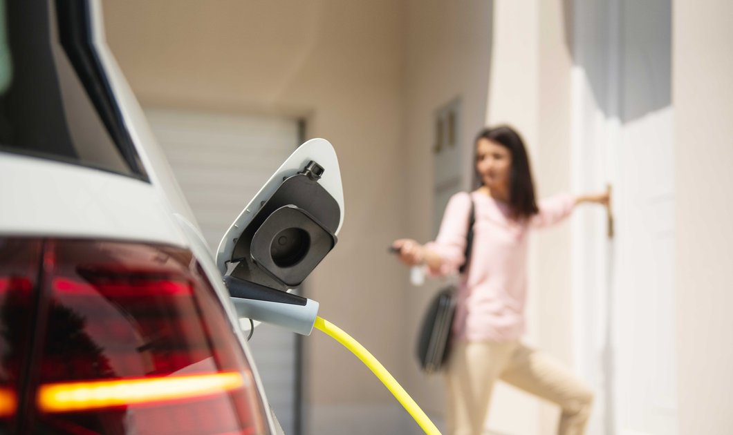 Parkendes E-Fahrzeug zur Aufladung mit Strom im Hintergund Person vor Haustür