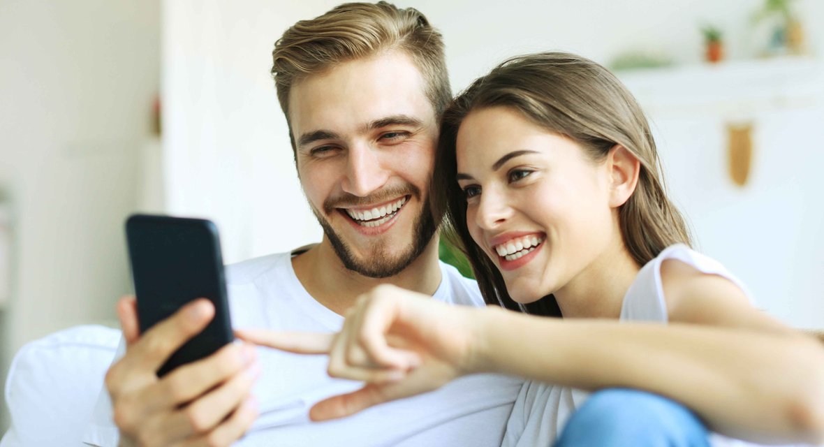 Zwei fröhliche Personen sitzend auf Mobiltelefon schauend